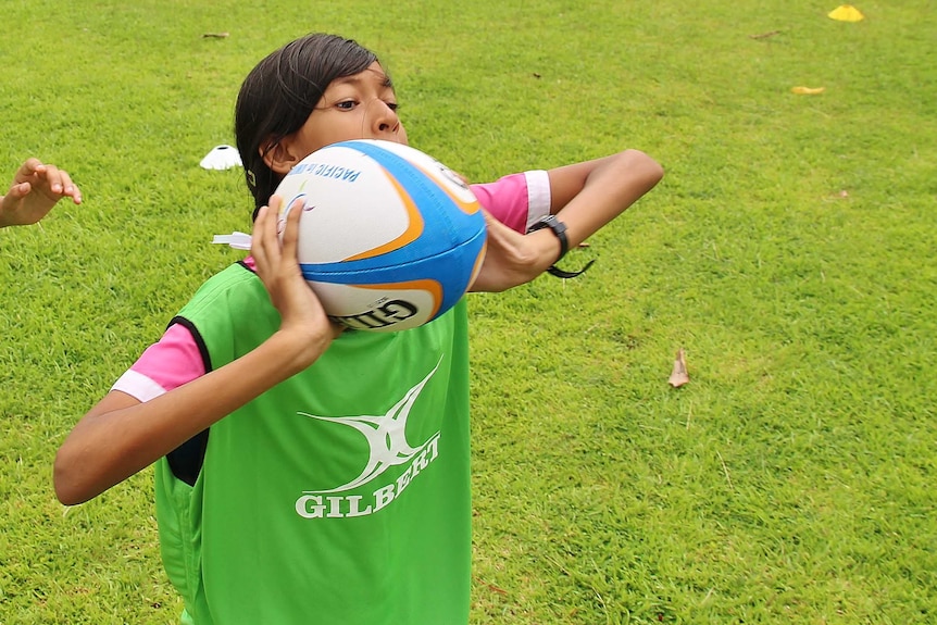 A young girl throws a rugby ball, her face partially obscured.