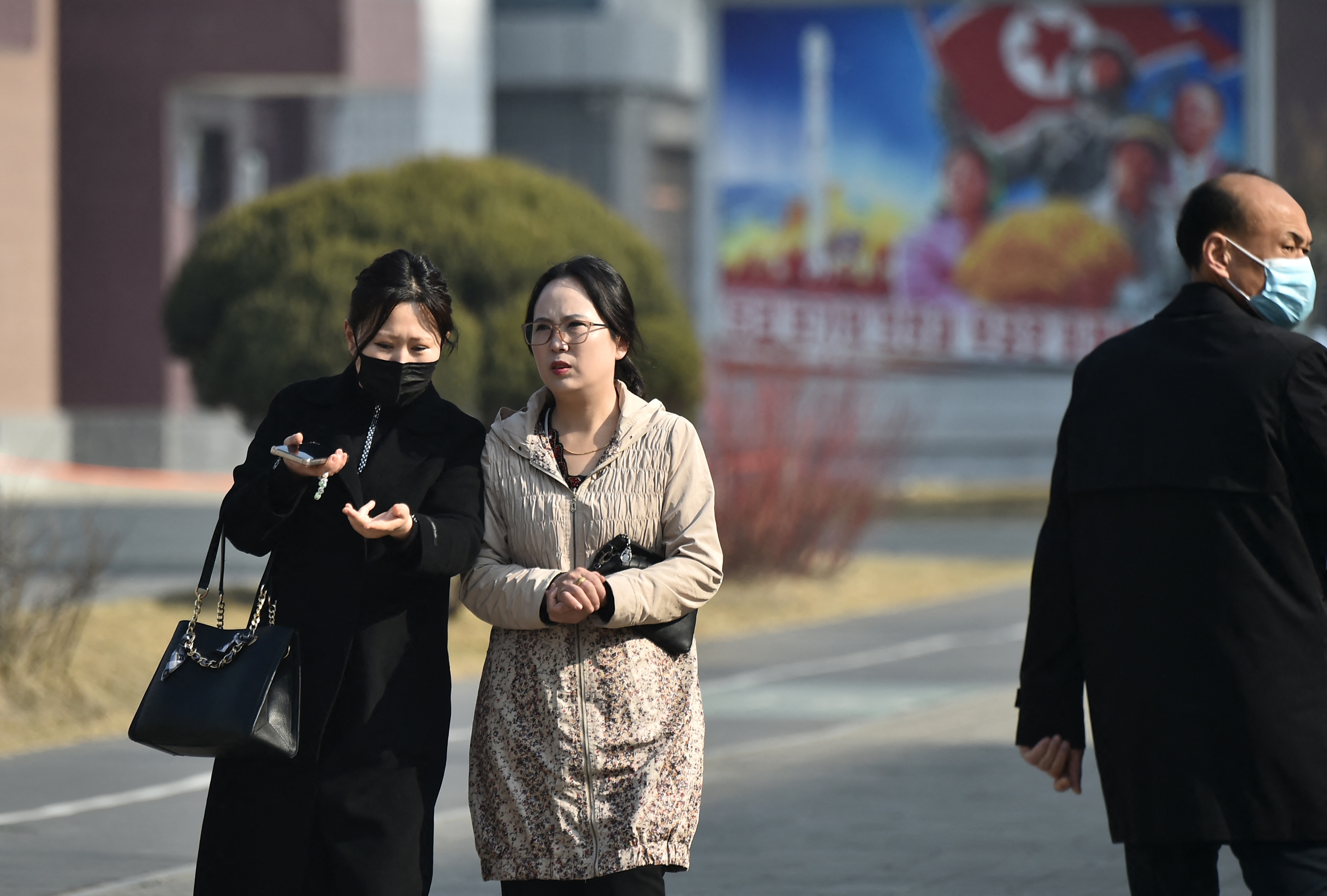 People walking along a North Korean street with a billboard in the background.