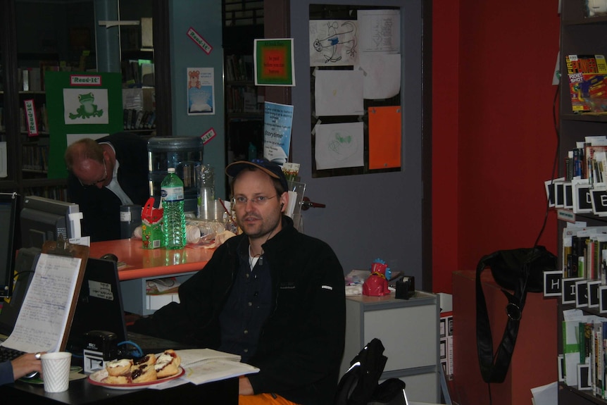 Vincent sitting at desk in library surrounded by children's books and artwork.