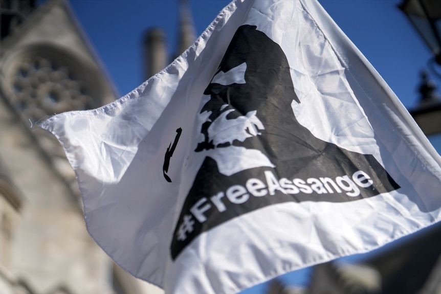 A flag with a silhouette of a man on it, and the word #FreeAssange near a large, grand building