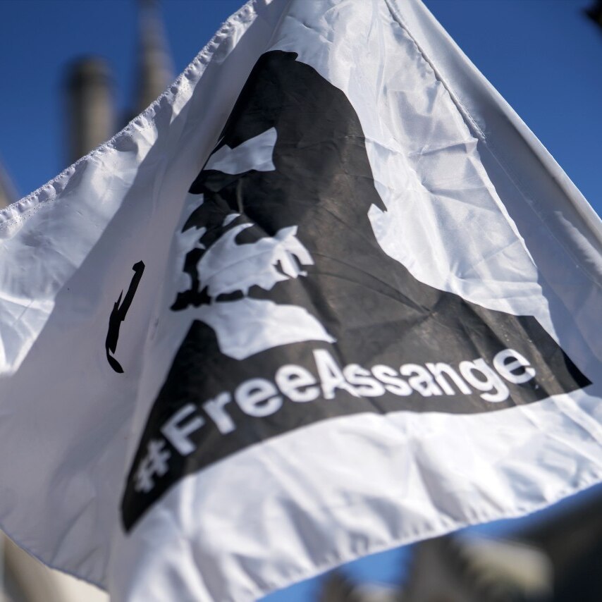 A flag with a silhouette of a man on it, and the word #FreeAssange near a large, grand building