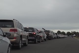 A long line of cars on a road leading to a small white tent.