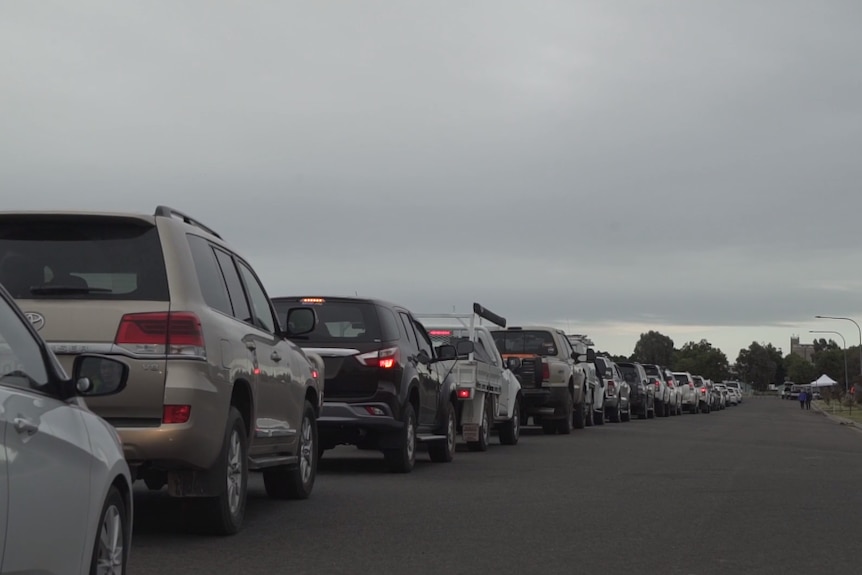 A long line of cars on a road leading to a small white tent.