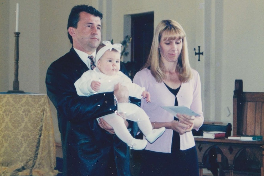 A man and woman stand in a church and hold their baby.
