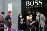 People wearing protective face masks stand in line to scan a barcode before entering a shopping mall.