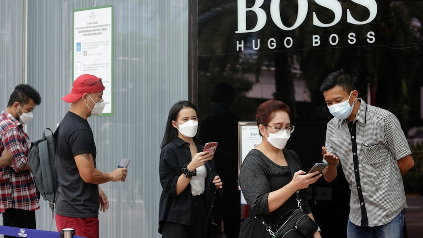 People wearing protective face masks stand in line to scan a barcode before entering a shopping mall.