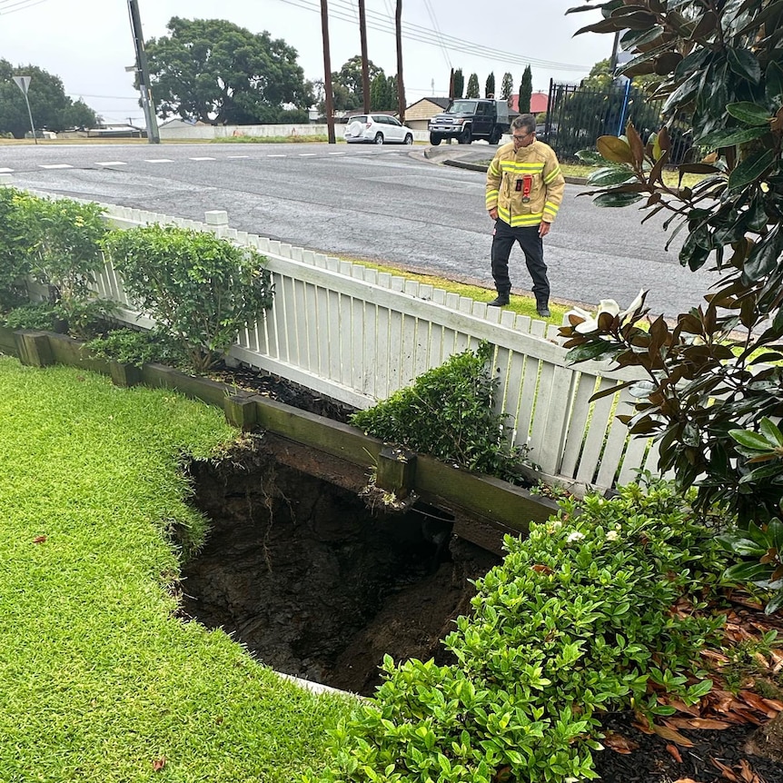A fire fighter stands over a large sinkhole, where part of a backyard and a white picket fence has fallen in