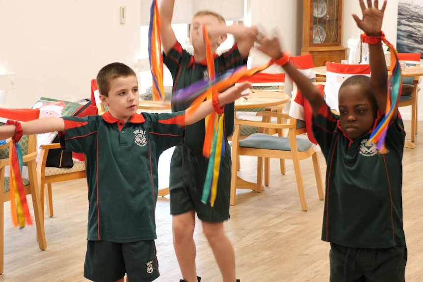 Three young boys perform in a nursing home, arms waving with streamers.