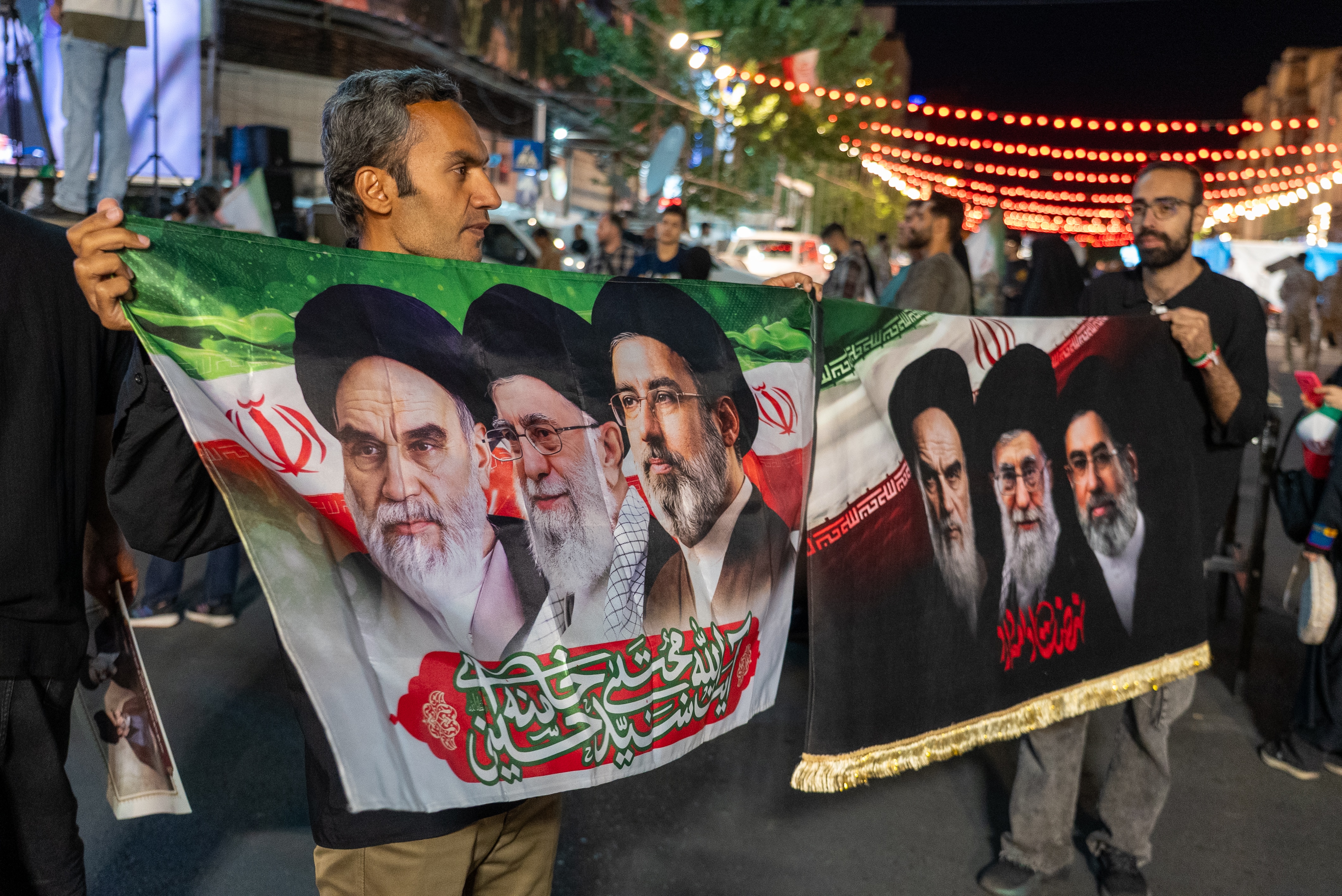 Two men holding flags featuring Iran's Supreme Leaders.