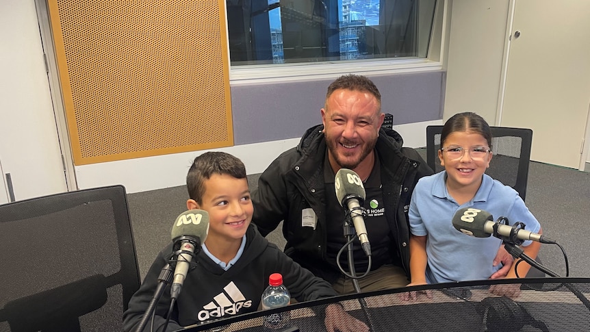Man and two children sit at microphones smiling