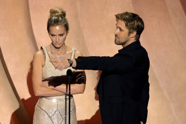 Emily Blunt with her arms crossed while Ryan Gosling points to the right. 