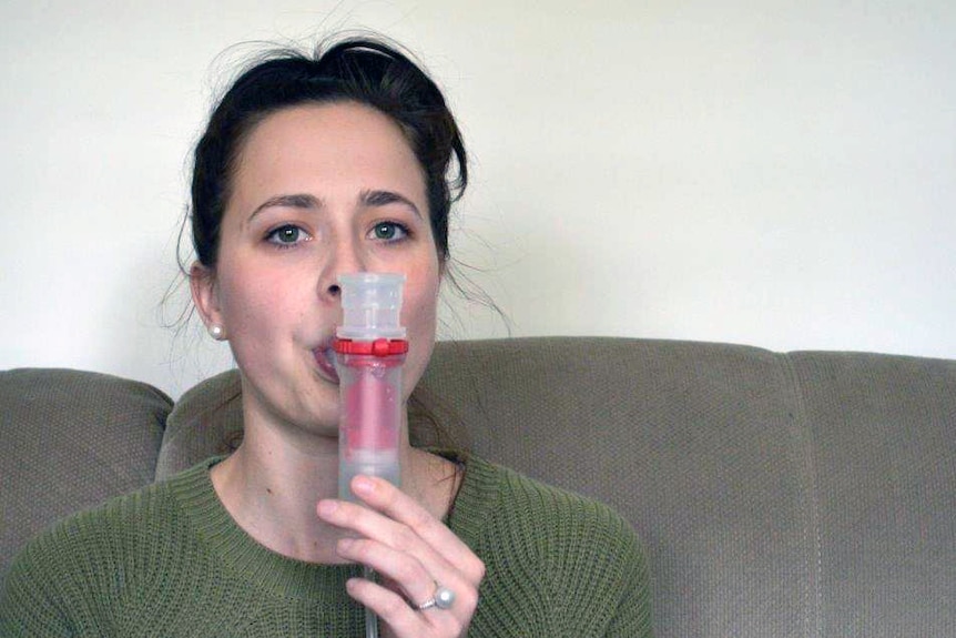 Jackie Hodson uses a nebulizer while sitting on a couch.