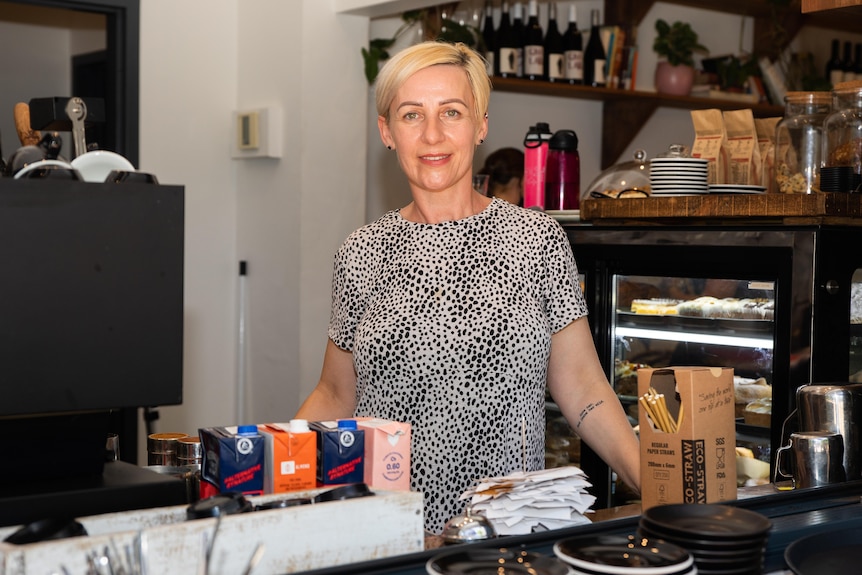 A woman standing in a cafe next to a coffee machine.