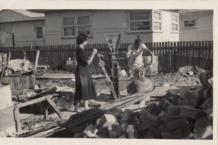 A black and white picture of a man and woman surrounded by building materials.