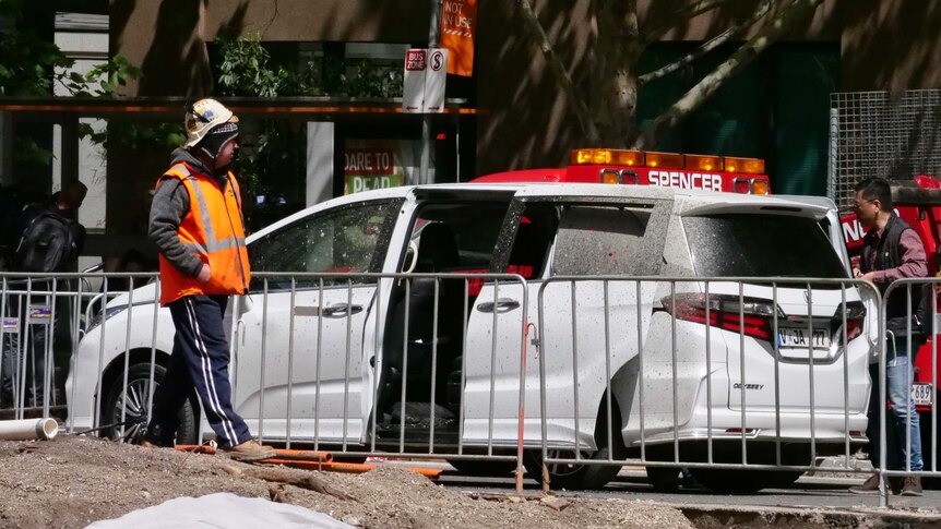 A worker looks at a car damaged by the sprayed concrete.