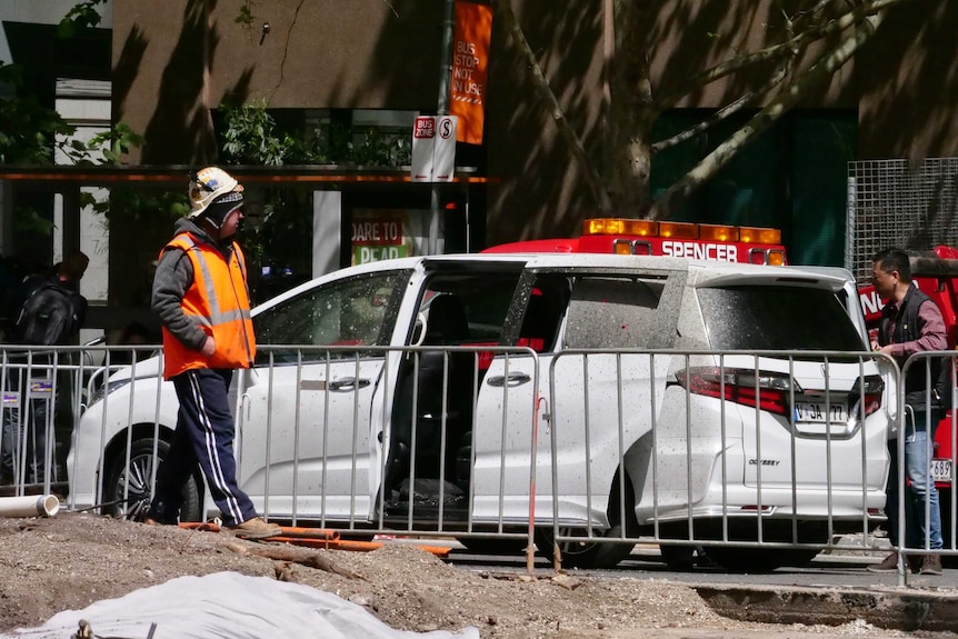 A worker looks at a car damaged by the sprayed concrete.