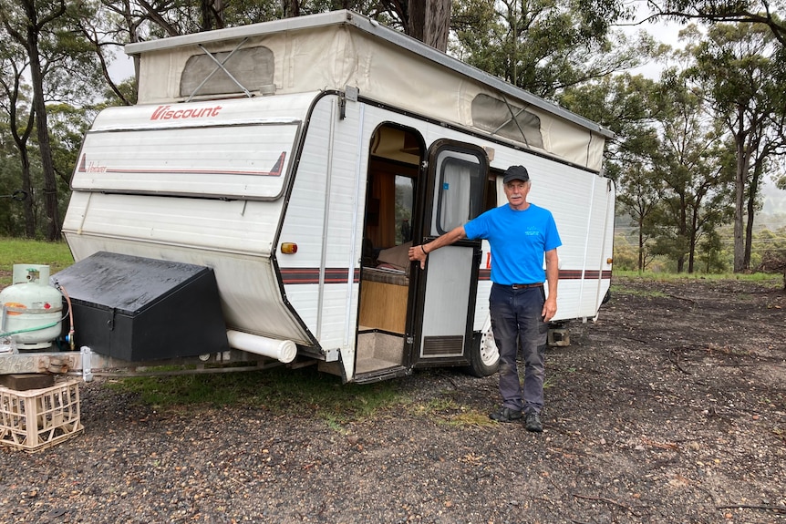 A man in a blue shirt standing next to a caravan.