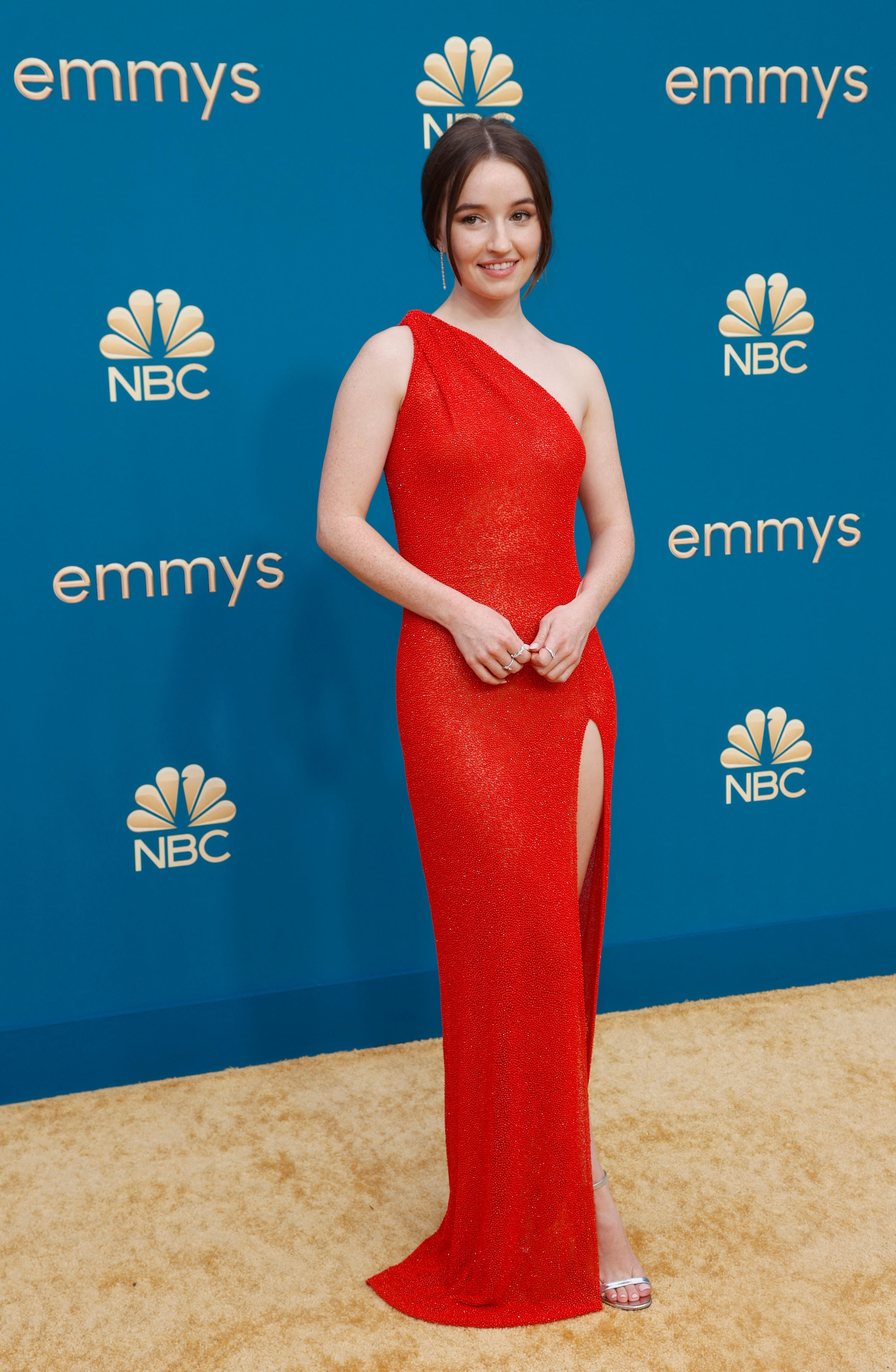 Kaitlyn Dever wears a red one-shoulder dress with a high thigh split