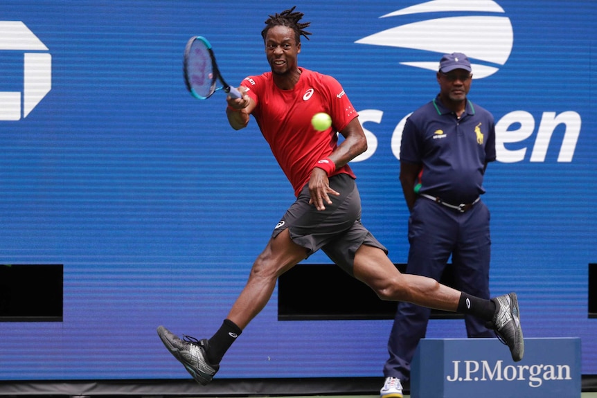 A male tennis player runs to his right with his right arm outstretched holding a racquet as he plays a forehand stroke.