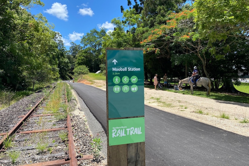 signage on rail trail pointing to Mooball Station; horse and bike riders off track in background