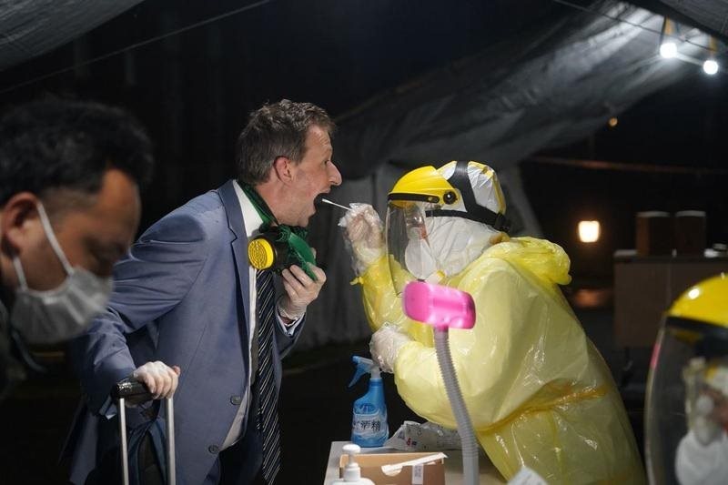 A man in protective gear is putting a cotton swab down a man's throat.