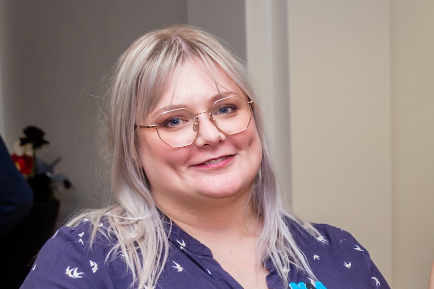 A woman in a blue and white patterned dress smiles at the camera   