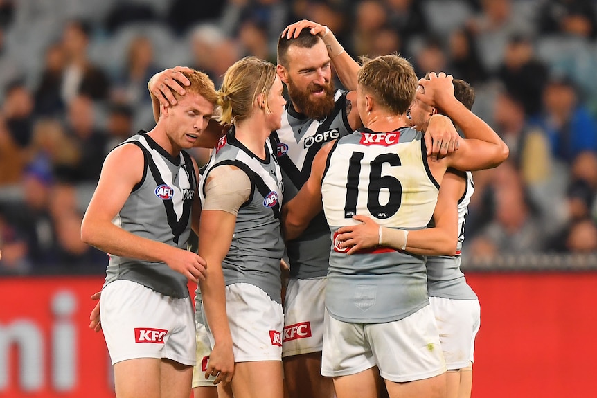 Five Port Adelaide Power AFL players embrace as they celebrate a goal.
