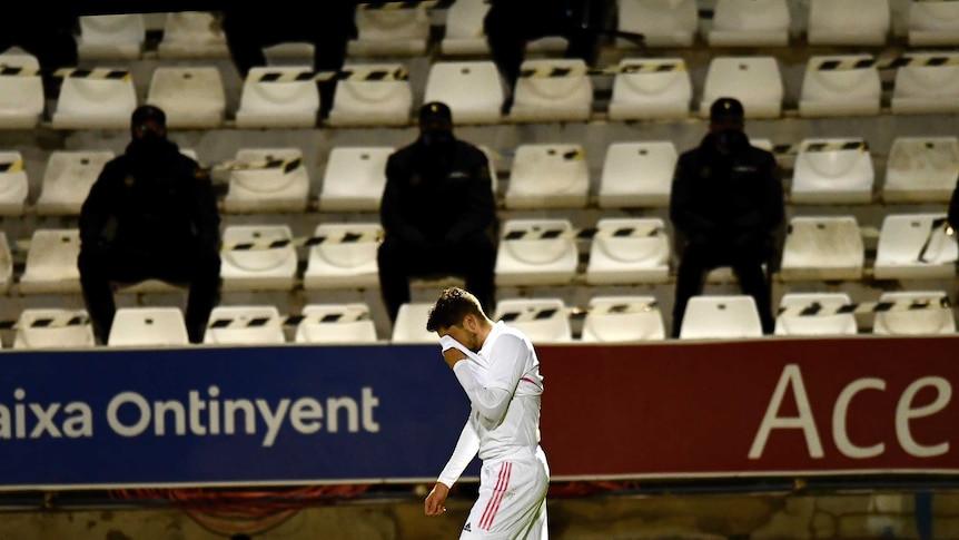 Federico Valverde puts his face in his shirt as dark figures look on from the stands.