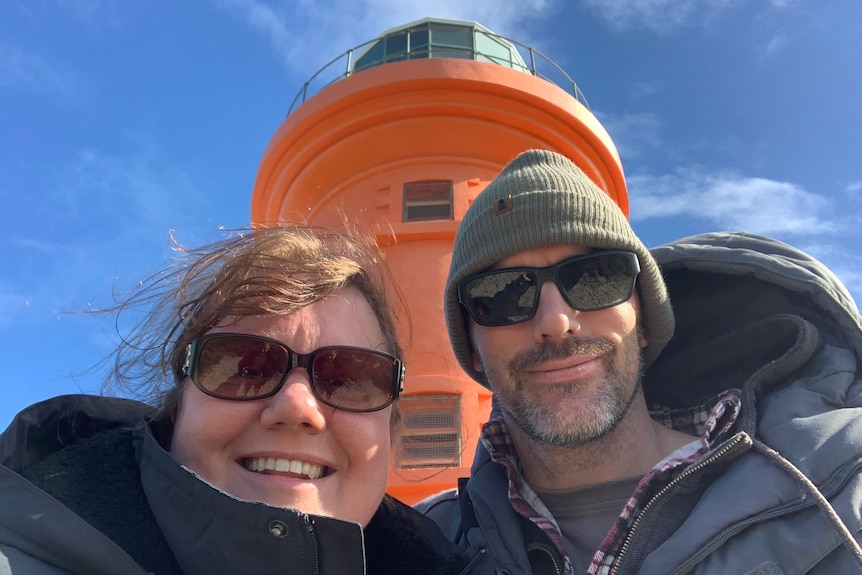 Woman and man dressed in cold weather gear in front of a lighthouse.