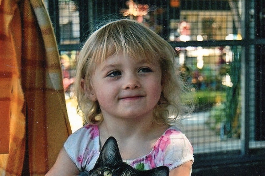 A little blonde girl smiles while holding a black cat