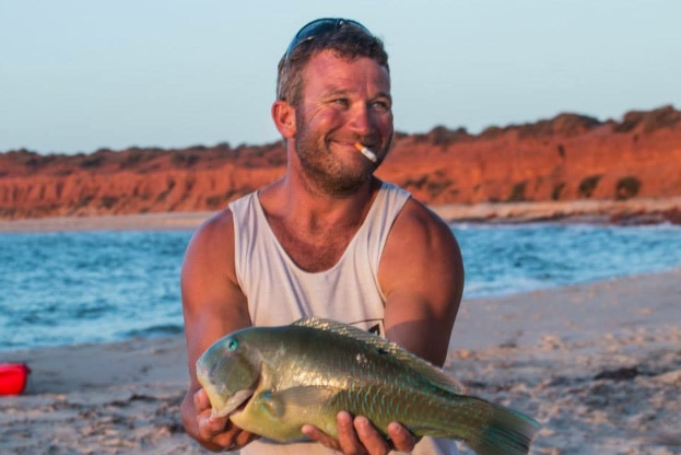 A picture of Luke Anthony Murray on a beach holding a fish.