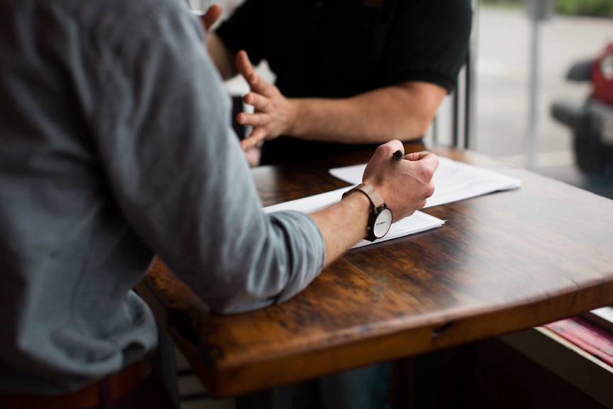 Two people sitting across a table talk about business.