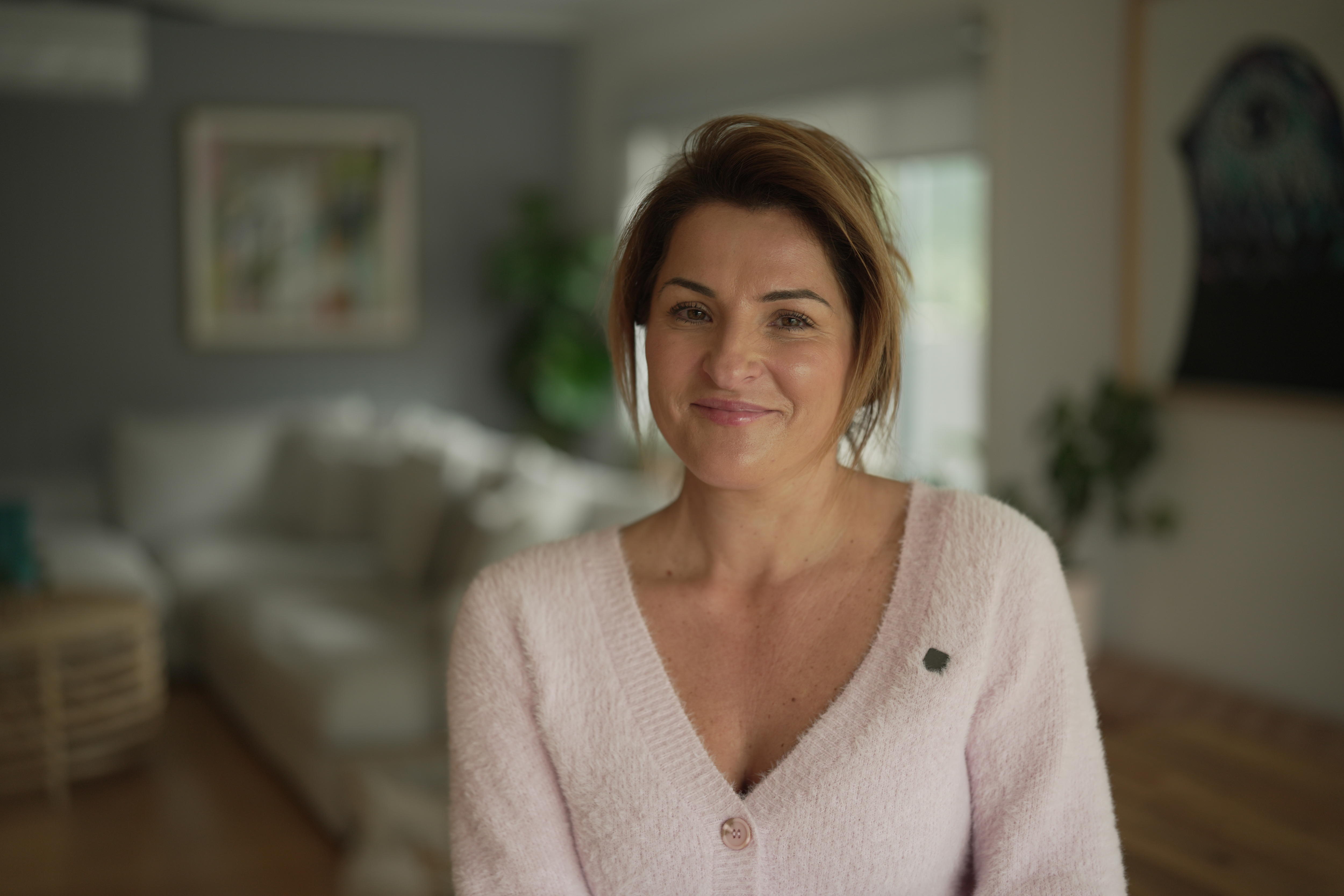 A young mum with brown hair sitting in a living room smiling