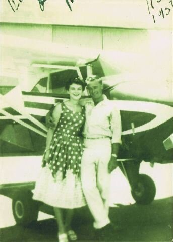 An old photo of a young couple standing next to a small plane