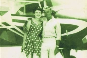 An old photo of a young couple standing next to a small plane