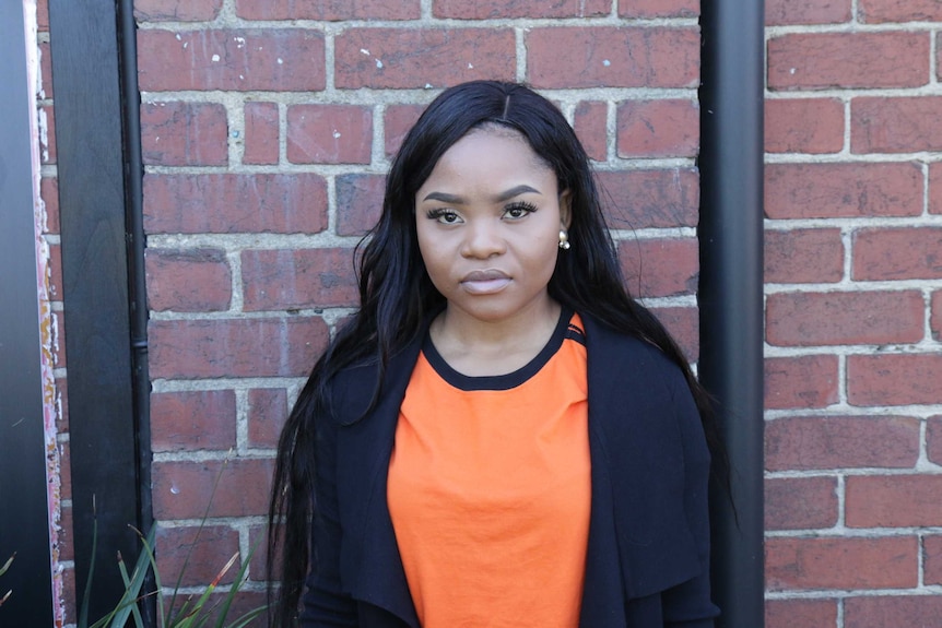 A young black woman, looking a bit sad and concerned, poses in front of a brick wall