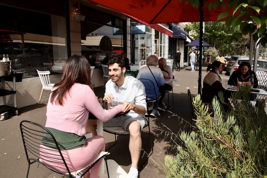 Eight diners sit at tables on the footpath outside a Melbourne cafe.