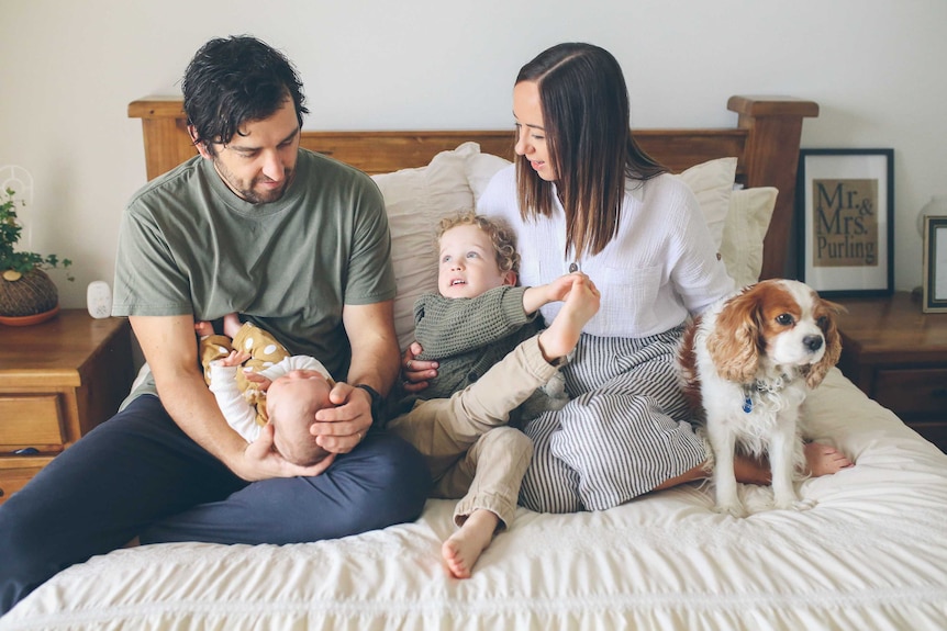 Amy Purling sitting on a bed with her husband, two children and dog