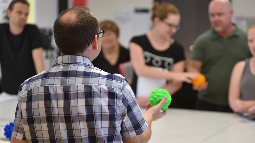 Dr Padraig Strappe teaching a class, holding a 3d printed plastic virus.