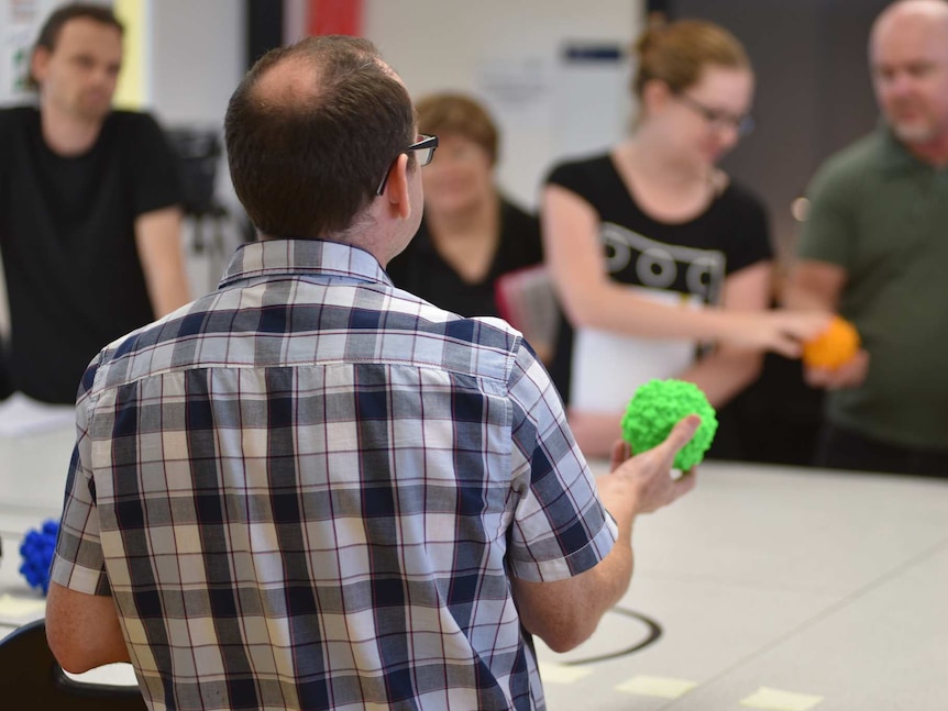 Dr Padraig Strappe teaching a class, holding a 3d printed plastic virus.