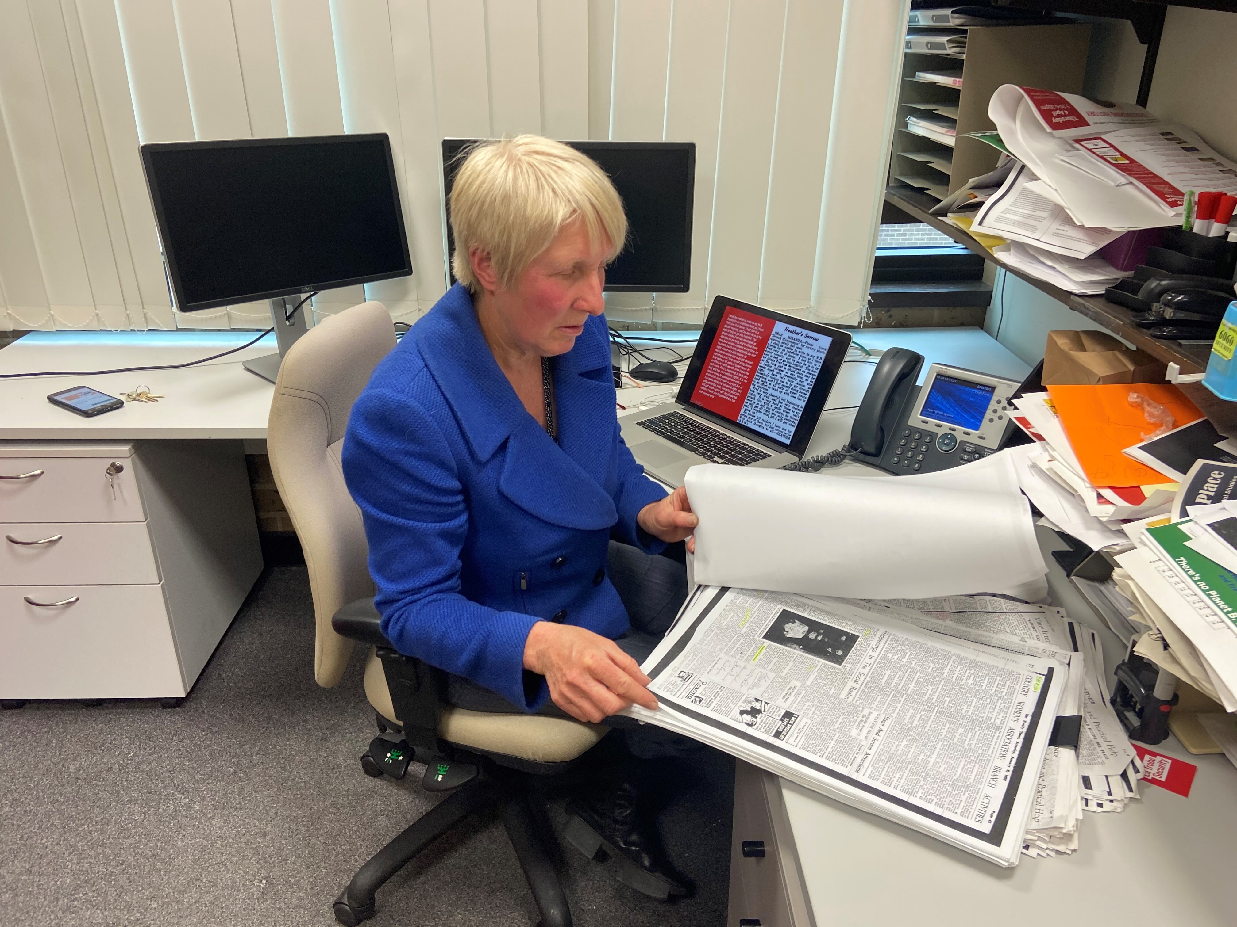 A lady sitting at a desk, reading big letters. 