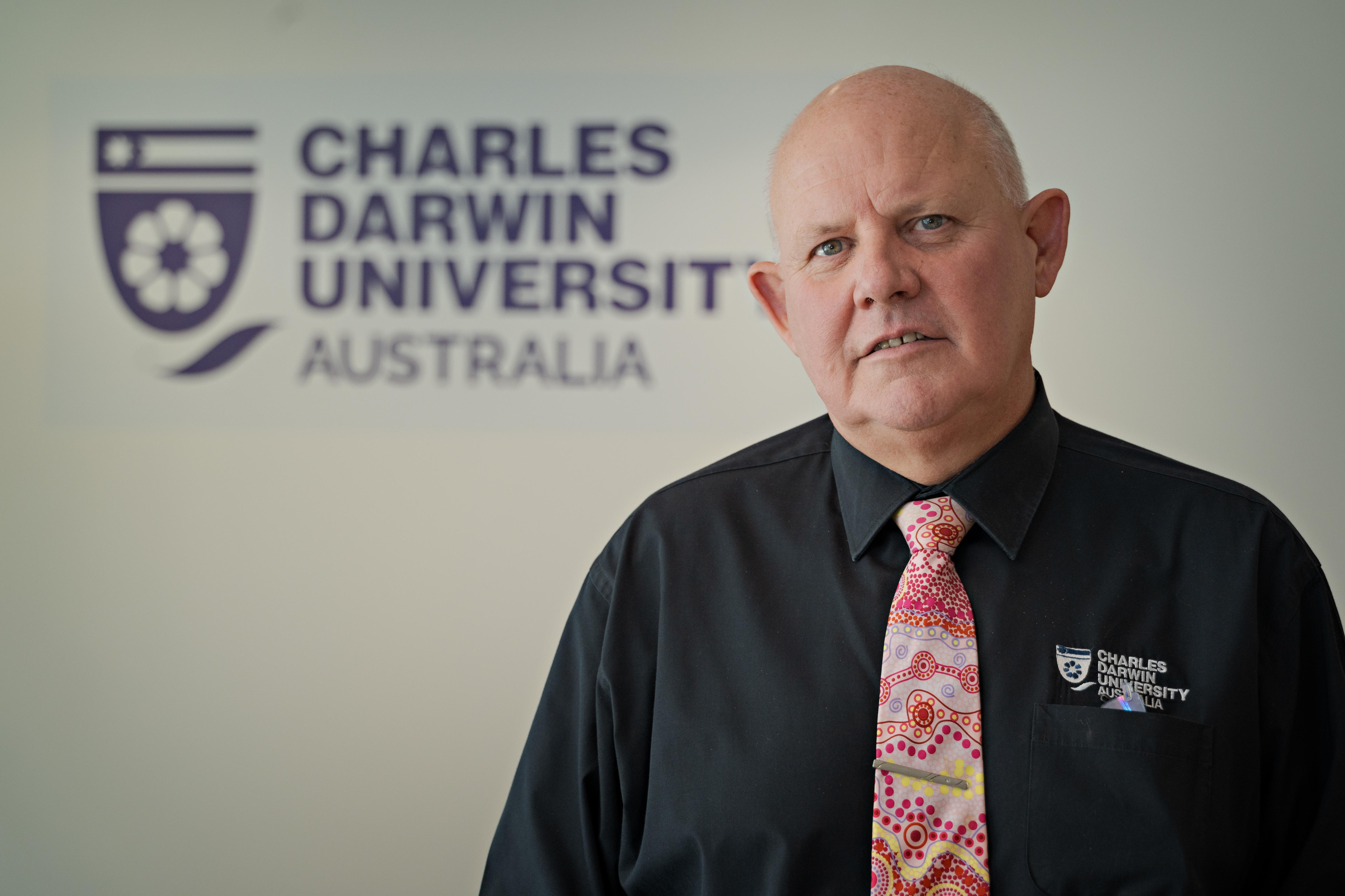 Un primer plano de un hombre calvo con camisa negra y corbata estampada.