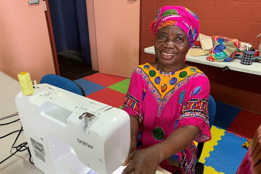 Congo refugee Riziki Ramadhani sits behind a sewing machine with bright pink dress and head scarf.