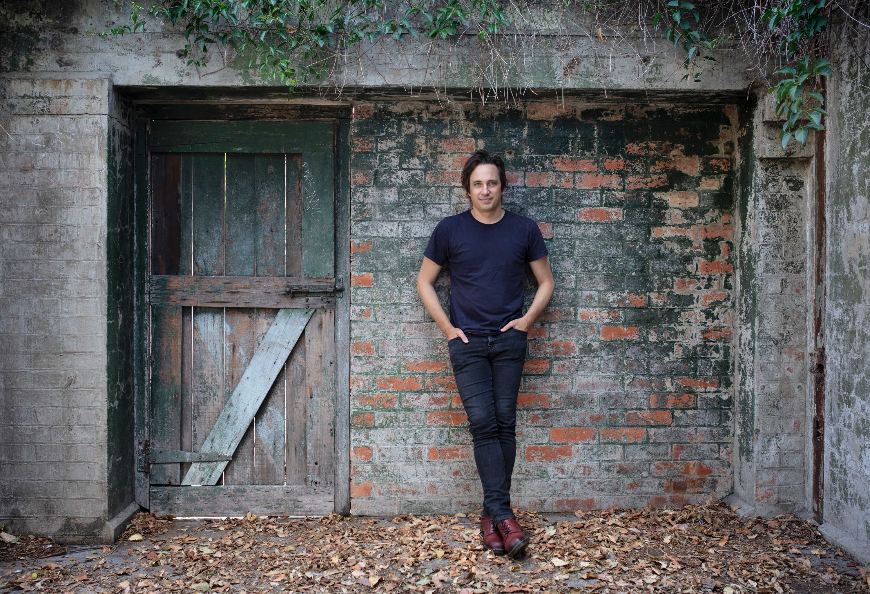 Man in dark clothes leans against old brick wall