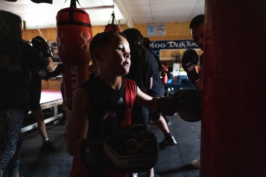 A young girl is working on a heavy bag in a boxing gym.