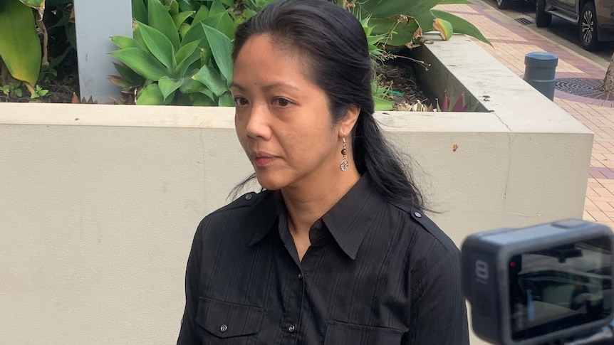 A woman of Asian heritage, dressed in black, looks solemn as she arrives at court.