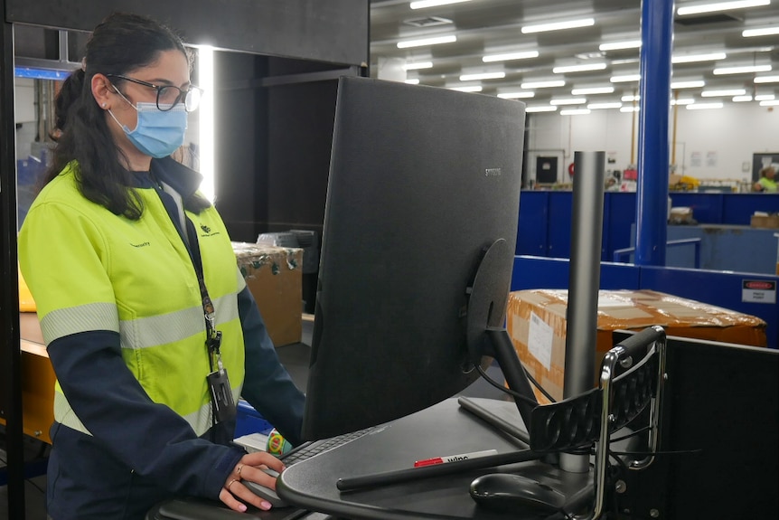 A woman in a mask and fluorescent yellow jumper looking at a computer