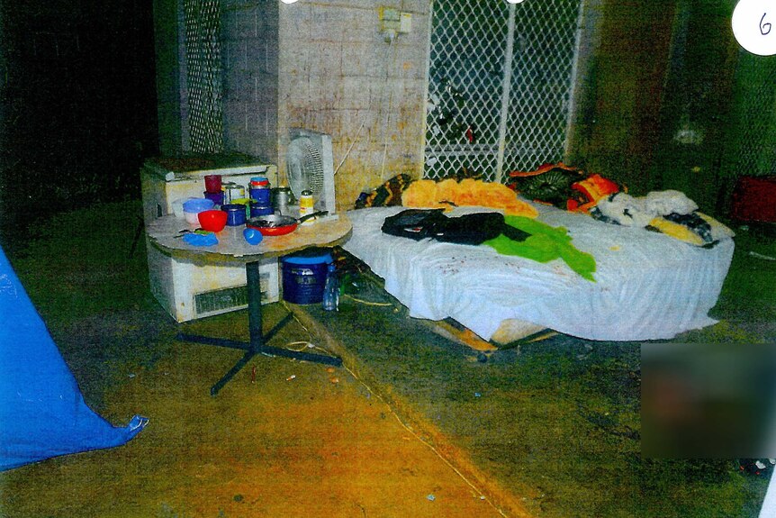 A squalid looking area with a mattress  and kitchen items.