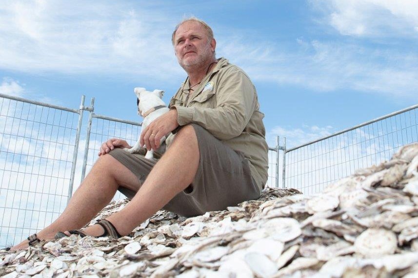 Robbie Porter sitting on a pile of cleaned shells with his dog.