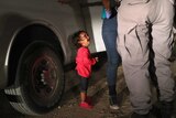 A child in a pink shirt cries and looks up at her mother, who is being detained by officials near the US-Mexico border.